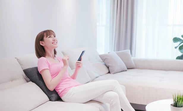 Woman sitting on couch uses smartphone to control smart home devices