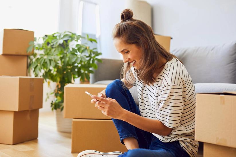 Woman texting while sitting in front of packed boxes in apartment