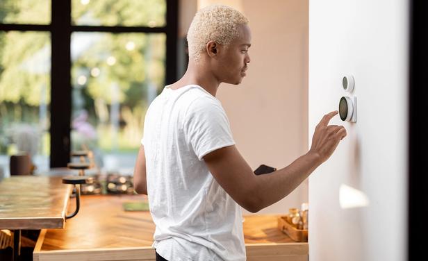Young adult adjusts his smart thermostat. 