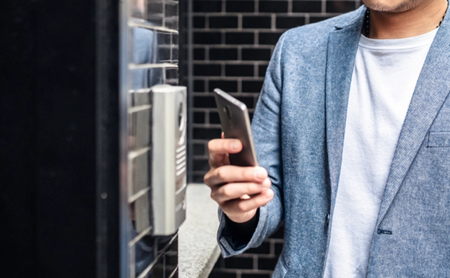 man outside building holding phone next to access reader
