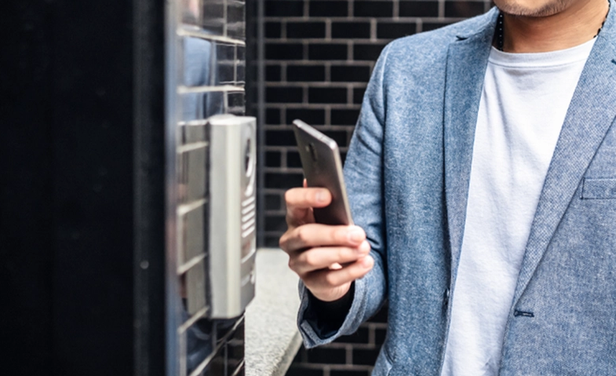 man outside building holding phone next to access reader
