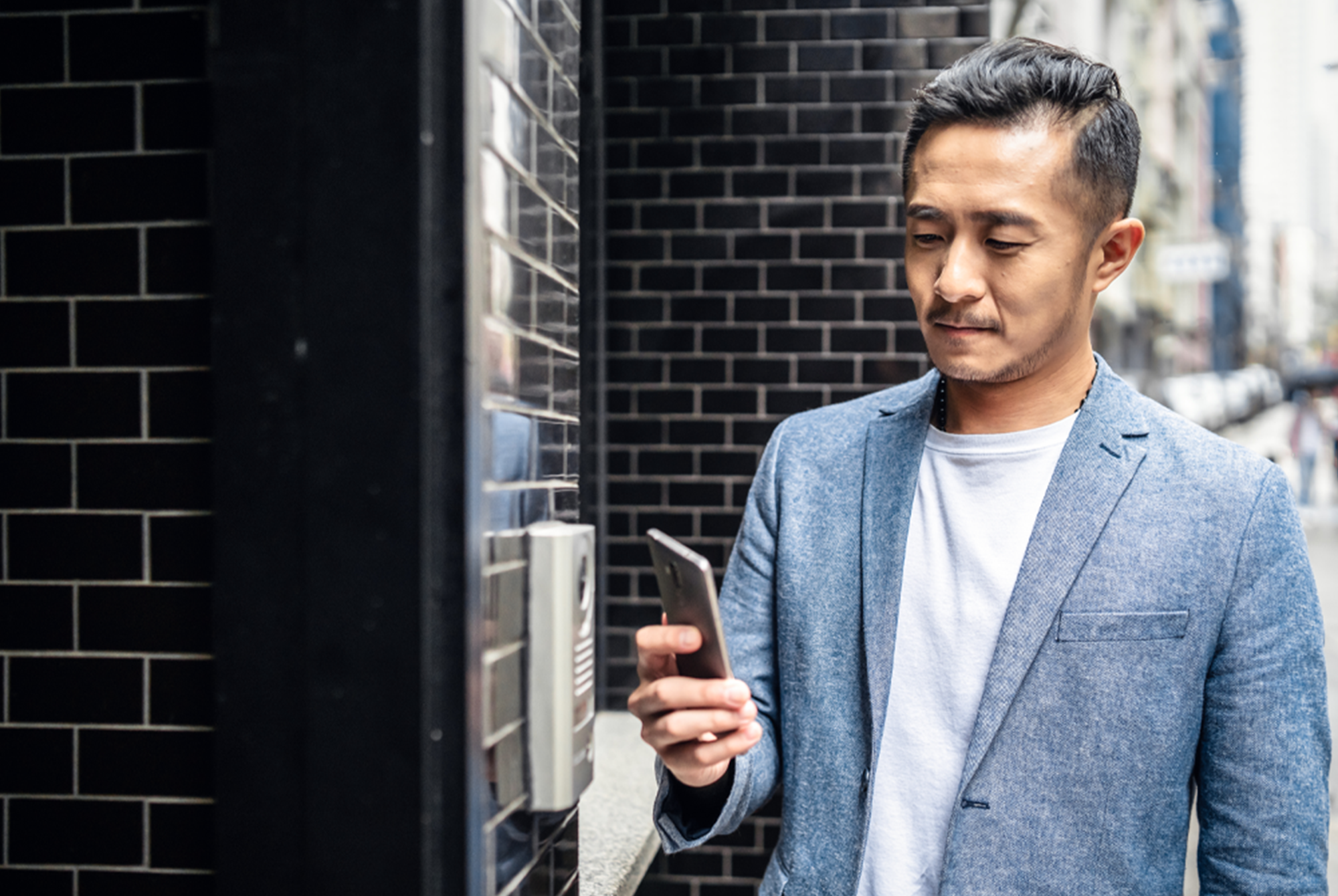 man outside building holding phone next to access reader