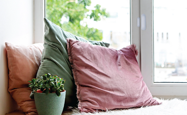 close up of contact sensor mounted on a window with bench and pillows below